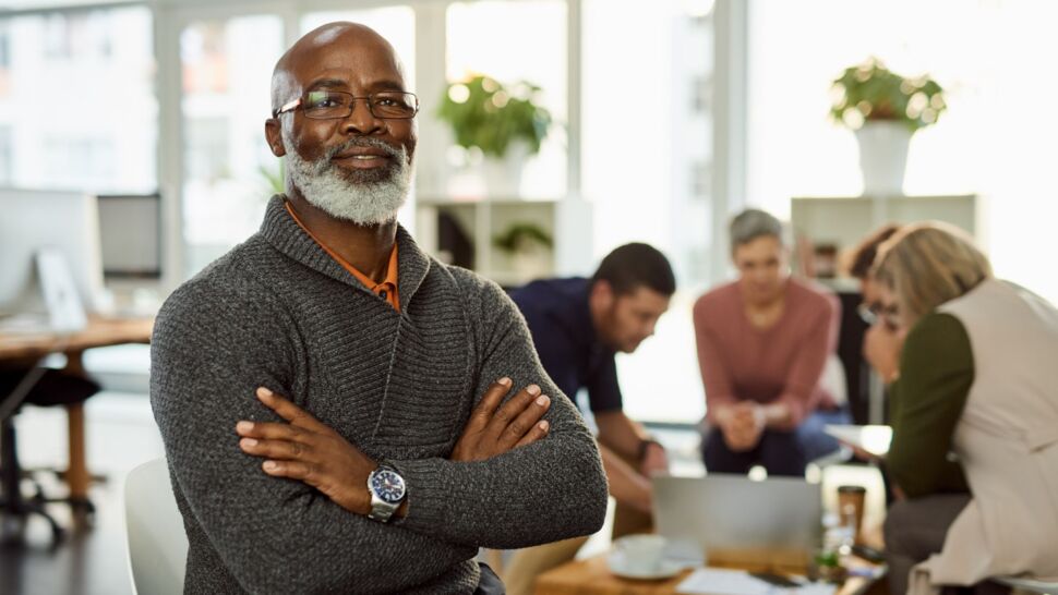 man-with-arms-crossed-sitting-in-front-of-his-team